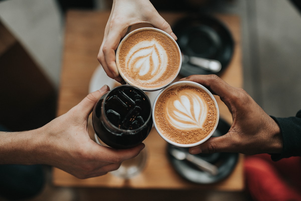 Three people raising coffee cups together over a table